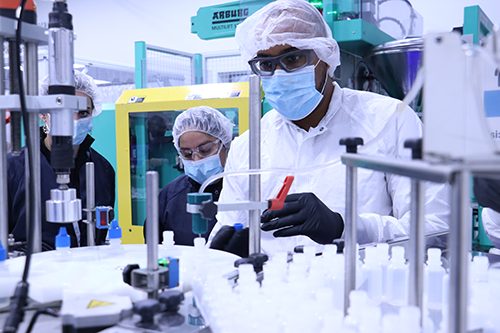 Engineers and operators watching semi-automated liquid bottle filling and sealing line run