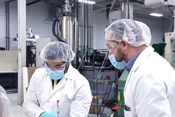 2 engineers wearing facemasks looking at an injection molded part