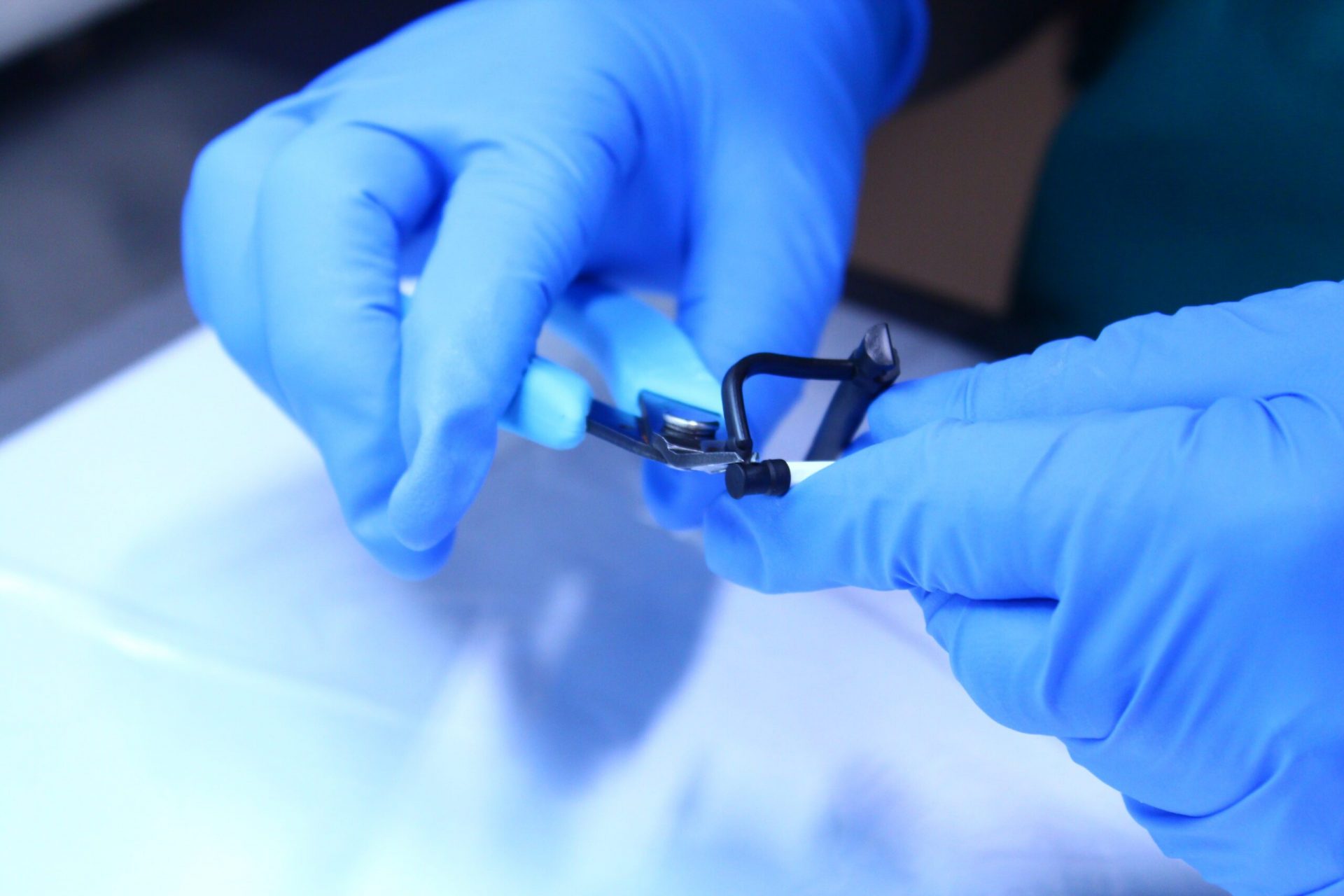 A pair of hands wearing gloves and using clippers on an injection molded part