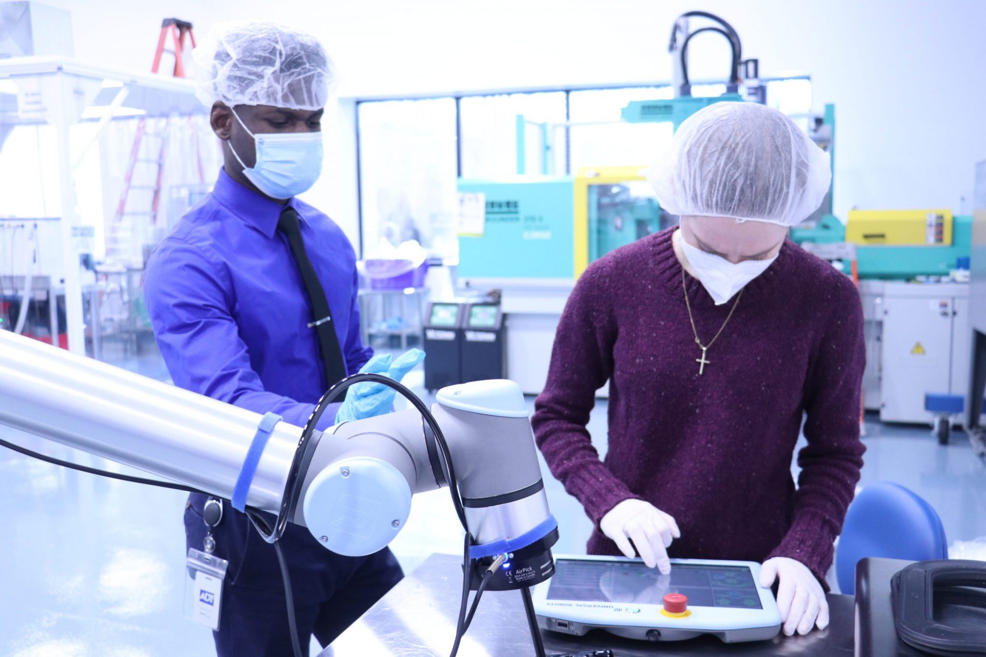 Two engineers with facemasks and hairnets in a lab looking at a tablet